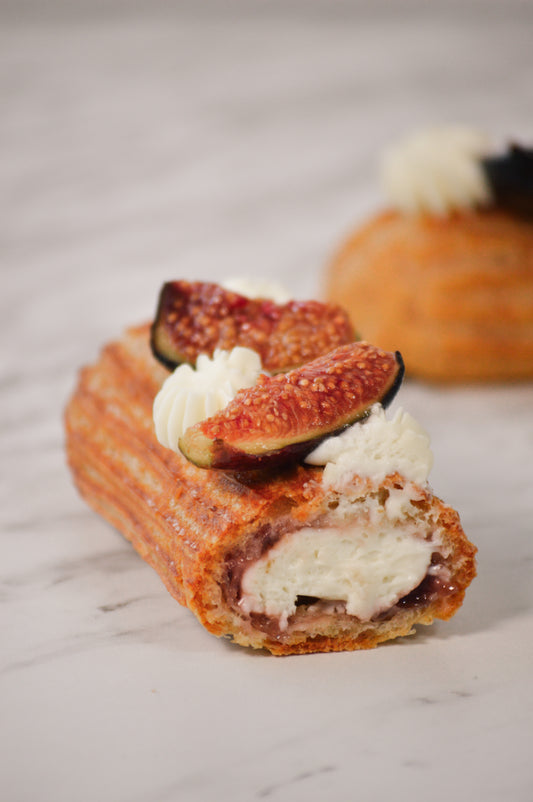 Éclair de higo con queso de cabra, visto de frente, sobre pâte à choux dorada con crema y pedacitos de higo fresco.